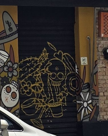 Porta de enrolar preta com uma calavera, cactos e flores desenhados em traço dourado.